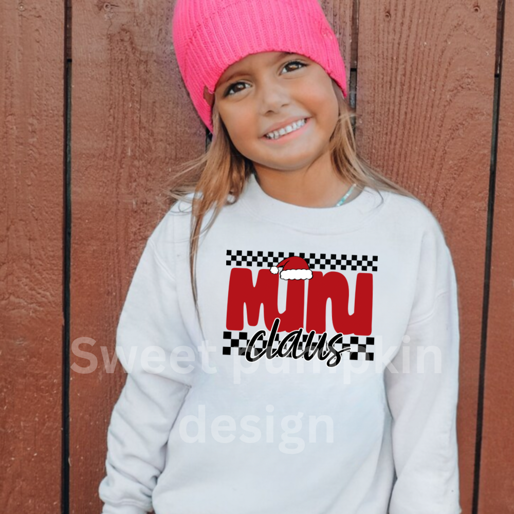 Child wearing a white sweatshirt with 'Mini Claus' text, pink beanie, against a wooden background
