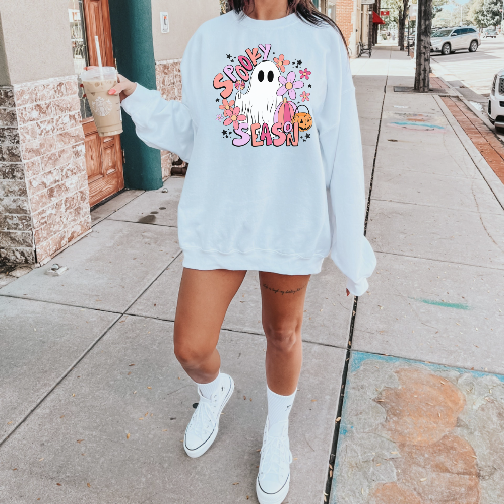 A trendy and oversized Halloween sweatshirt in pink, featuring a cute ghost design with the text 'Spooky Season'. This pastel pink fall sweatshirt adds a playful touch to your autumn wardrobe.