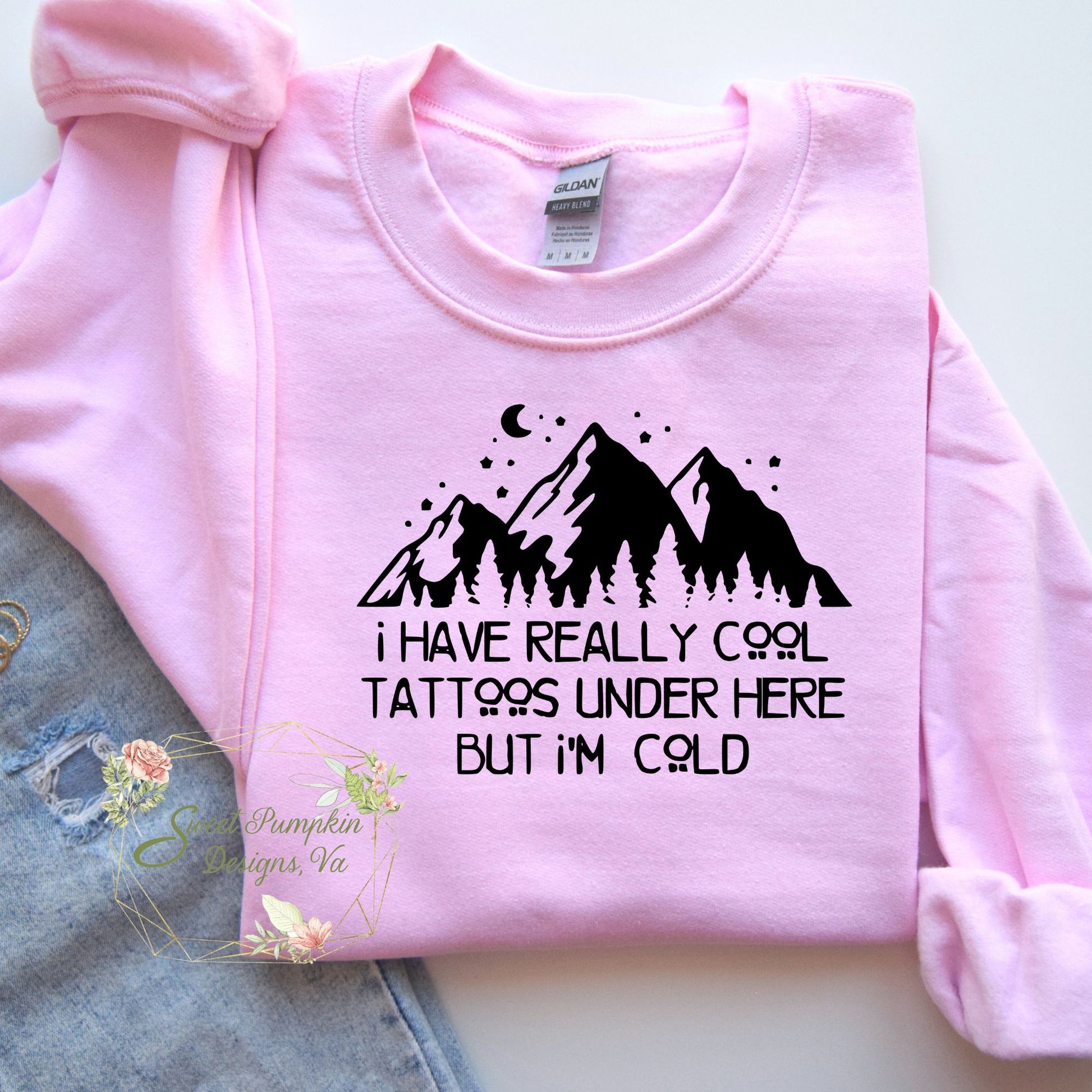 A trendy crewneck sweatshirt with a humorous graphic that reads 'I have really cool tattoos under here but I'm cold'. The graphic features bold typography. The sweatshirt is made from a soft and comfortable cotton blend and features ribbed cuffs and hem. It has a regular fit and a crewneck design.